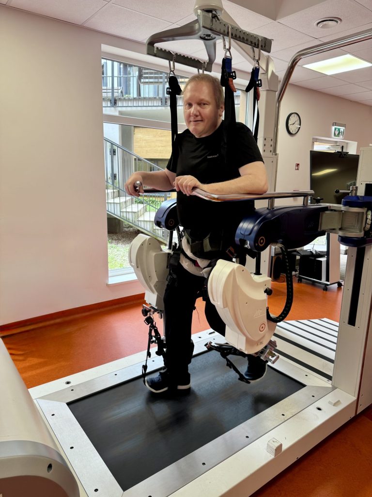 Reedukcja chodu podczas rehabilitacji po udarze z wykorzystaniem robota wspomagającego. Pacjent ćwiczy na bieżni w specjalistycznym systemie podwieszenia i stabilizacji, który wspiera prawidłowy wzorzec ruchu oraz poprawę samodzielnego chodzenia